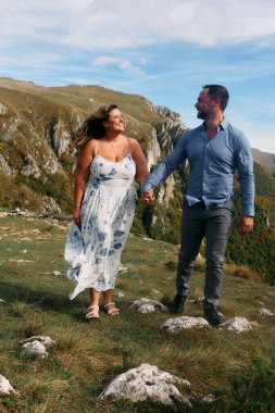 Sonbahar boyunca manzaralı bir dağ yolunda el ele yürüyen çift, doğanın tadını çıkarıyor ve birbirlerine eşlik ediyorlar..