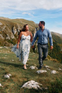 Sonbahar boyunca manzaralı bir dağ yolunda el ele yürüyen çift, doğanın tadını çıkarıyor ve birbirlerine eşlik ediyorlar..