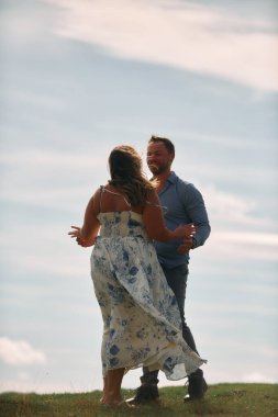 Çimenli bir dağ tarlasında neşeli bir şekilde dans eden erkek ve kadın aydınlık bir günde, doğada sevgi ve özgürlüğün tadını çıkarıyorlar..