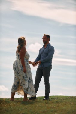 Çimenli bir dağ tarlasında neşeli bir şekilde dans eden erkek ve kadın aydınlık bir günde, doğada sevgi ve özgürlüğün tadını çıkarıyorlar..