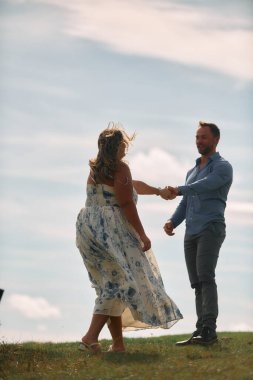 Çimenli bir dağ tarlasında neşeli bir şekilde dans eden erkek ve kadın aydınlık bir günde, doğada sevgi ve özgürlüğün tadını çıkarıyorlar..