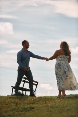 Çimenli bir dağ tarlasında neşeli bir şekilde dans eden erkek ve kadın aydınlık bir günde, doğada sevgi ve özgürlüğün tadını çıkarıyorlar..