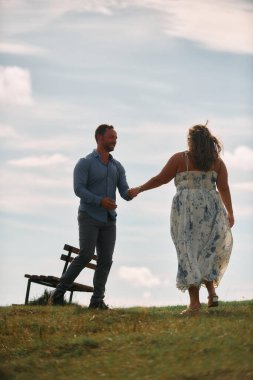 Çimenli bir dağ tarlasında neşeli bir şekilde dans eden erkek ve kadın aydınlık bir günde, doğada sevgi ve özgürlüğün tadını çıkarıyorlar..