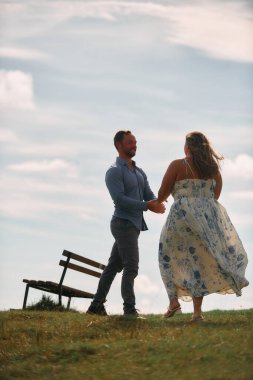 Çimenli bir dağ tarlasında neşeli bir şekilde dans eden erkek ve kadın aydınlık bir günde, doğada sevgi ve özgürlüğün tadını çıkarıyorlar..