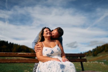 Erkek, dışarıda otururken partnerinin omzunu öper. Sevgisini, neşesini ve duygusal bağını gösterir..
