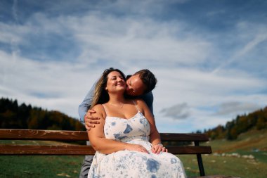 Erkek, dışarıda otururken partnerinin omzunu öper. Sevgisini, neşesini ve duygusal bağını gösterir..