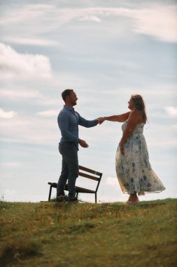 Çimenli bir dağ tarlasında neşeli bir şekilde dans eden erkek ve kadın aydınlık bir günde, doğada sevgi ve özgürlüğün tadını çıkarıyorlar..