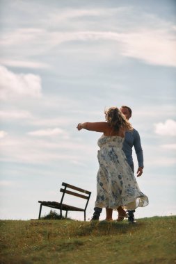 Çimenli bir dağ tarlasında neşeli bir şekilde dans eden erkek ve kadın aydınlık bir günde, doğada sevgi ve özgürlüğün tadını çıkarıyorlar..