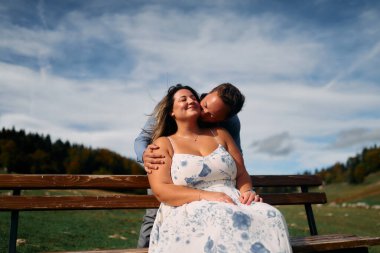 Erkek, dışarıda otururken partnerinin omzunu öper. Sevgisini, neşesini ve duygusal bağını gösterir..