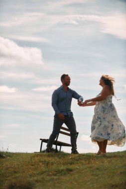 Çimenli bir dağ tarlasında neşeli bir şekilde dans eden erkek ve kadın aydınlık bir günde, doğada sevgi ve özgürlüğün tadını çıkarıyorlar..