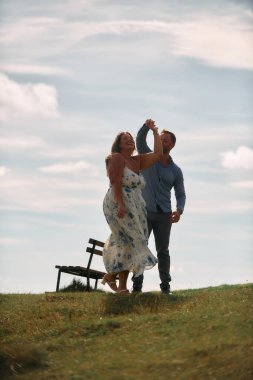 Çimenli bir dağ tarlasında neşeli bir şekilde dans eden erkek ve kadın aydınlık bir günde, doğada sevgi ve özgürlüğün tadını çıkarıyorlar..