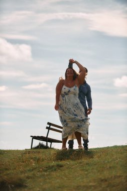 Çimenli bir dağ tarlasında neşeli bir şekilde dans eden erkek ve kadın aydınlık bir günde, doğada sevgi ve özgürlüğün tadını çıkarıyorlar..