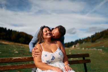 Erkek, dışarıda otururken partnerinin omzunu öper. Sevgisini, neşesini ve duygusal bağını gösterir..
