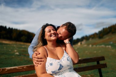 Erkek, dışarıda otururken partnerinin omzunu öper. Sevgisini, neşesini ve duygusal bağını gösterir..