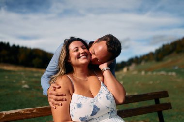 Erkek, dışarıda otururken partnerinin omzunu öper. Sevgisini, neşesini ve duygusal bağını gösterir..