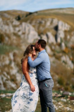 Rüzgarlı bir günde, dağlarda romantik bir anda gülümseyen kadını alnından öpen bir adam..