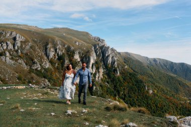 Sonbahar boyunca manzaralı bir dağ yolunda el ele yürüyen çift, doğanın tadını çıkarıyor ve birbirlerine eşlik ediyorlar..