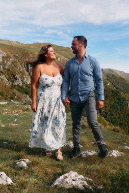 Sonbahar boyunca manzaralı bir dağ yolunda el ele yürüyen çift, doğanın tadını çıkarıyor ve birbirlerine eşlik ediyorlar..