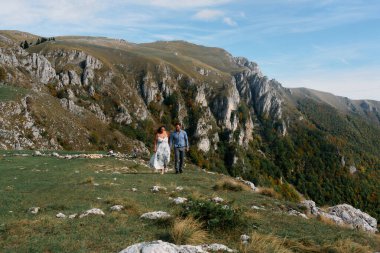 Sonbahar boyunca manzaralı bir dağ yolunda el ele yürüyen çift, doğanın tadını çıkarıyor ve birbirlerine eşlik ediyorlar..