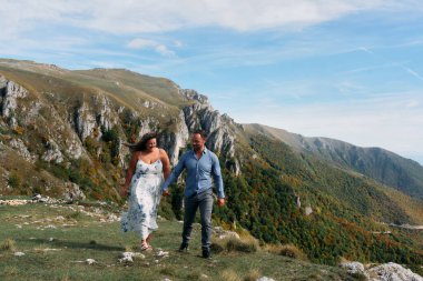 Sonbahar boyunca manzaralı bir dağ yolunda el ele yürüyen çift, doğanın tadını çıkarıyor ve birbirlerine eşlik ediyorlar..