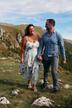 Sonbahar boyunca manzaralı bir dağ yolunda el ele yürüyen çift, doğanın tadını çıkarıyor ve birbirlerine eşlik ediyorlar..