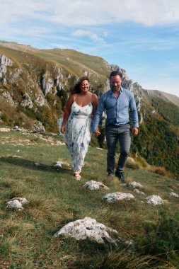 Sonbahar boyunca manzaralı bir dağ yolunda el ele yürüyen çift, doğanın tadını çıkarıyor ve birbirlerine eşlik ediyorlar..