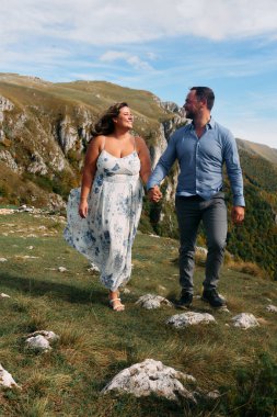 Sonbahar boyunca manzaralı bir dağ yolunda el ele yürüyen çift, doğanın tadını çıkarıyor ve birbirlerine eşlik ediyorlar..