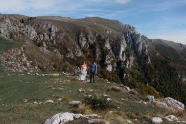Sonbahar boyunca manzaralı bir dağ yolunda el ele yürüyen çift, doğanın tadını çıkarıyor ve birbirlerine eşlik ediyorlar..