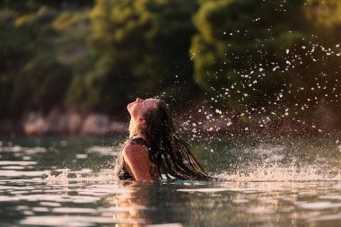 Plajda altın saat boyunca mayolu genç bir kadın ıslak saçlarını denize savuruyor. Gün batımında ıslak saçlarını suya atan bir kadın.