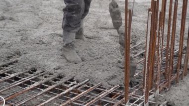 İnşaat işçisi inşaat alanındaki güçlendirilmiş çelik bir levhanın üzerine taze beton döküyor. Temel inşaatı sırasında el işçiliğini, güvenlik donanımını ve hassas çalışmayı gösteren endüstri sahnesi. 