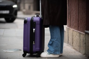 Mor bavul ve kadın bacaklarının detaylı görüntüsü şehir kaldırımında duruyor..