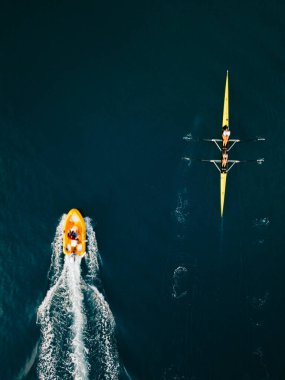 Koyu mavi denizde destek motorbotuyla çalışan bir kürek takımının hava aracı görüntüsü..
