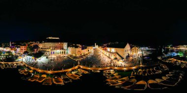 Hvar rıhtım meydanının canlı panoramik manzarası. Tekneler, tarihi taş binalar ve hareketli kalabalık..