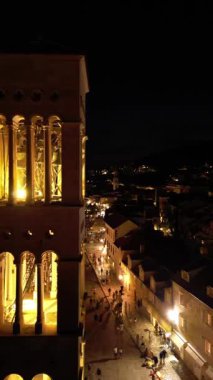 Restoranlar, insanlar ve aydınlatılmış katedrallerle dolu canlı Hvar şehir meydanının hava dikey gece videosu.