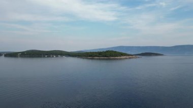 Parçalı bulutlu bir günde ormanlar ve tepelerle Hvar kasabasına yaklaşan insansız hava aracı videosu..