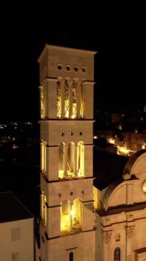Restoranlar, insanlar ve aydınlatılmış katedrallerle dolu canlı Hvar şehir meydanının hava dikey gece videosu.