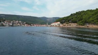 Parçalı bulutlu bir günde ormanlar ve tepelerle Hvar kasabasına yaklaşan insansız hava aracı videosu..