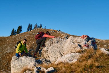Mountain Trail 'de çift yürüyüşü. Güneşli bir günde dağda kayalık patikaya tırmanan sırt çantalı iki yürüyüşçü, takım çalışması ve macera konsepti