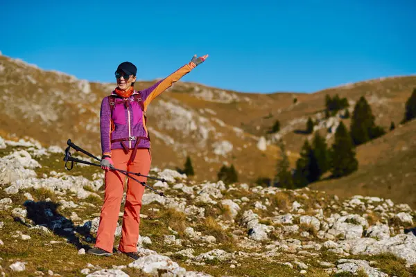 Sırt çantalı kadın yürüyüşçünün portresi. Renkli kıyafetler giyen kadın yürüyüşçünün portresi ve dağ manzarasında yürüyüş direkleri tutan güneş gözlüğü.