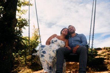 Dağlarda salıncakta sallanan bir çift, arka planda büyüleyici doğal manzarayla öpüşüyorlar. Seyahat, romantizm, yaşam tarzı ve macera temaları için mükemmel