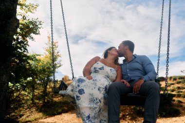 Dağlarda salıncakta sallanan bir çift, arka planda büyüleyici doğal manzarayla öpüşüyorlar. Seyahat, romantizm, yaşam tarzı ve macera temaları için mükemmel
