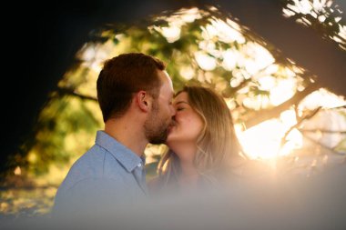 Genç çift, sıcak akşam güneşinde romantik bir öpücük paylaşıyor. Aşkı, samimiyeti ve mutluluğu simgeliyor. Yaşam tarzı, ilişki ve sevgililer günü temaları için mükemmel.