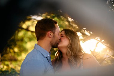 Genç çift, sıcak akşam güneşinde romantik bir öpücük paylaşıyor. Aşkı, samimiyeti ve mutluluğu simgeliyor. Yaşam tarzı, ilişki ve sevgililer günü temaları için mükemmel.