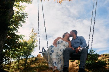 Dağlarda salıncakta sallanan bir çift, arka planda büyüleyici doğal manzarayla öpüşüyorlar. Seyahat, romantizm, yaşam tarzı ve macera temaları için mükemmel