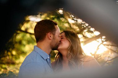 Genç çift, sıcak akşam güneşinde romantik bir öpücük paylaşıyor. Aşkı, samimiyeti ve mutluluğu simgeliyor. Yaşam tarzı, ilişki ve sevgililer günü temaları için mükemmel.