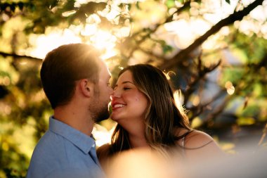 Genç çift, sıcak akşam güneşinde romantik bir öpücük paylaşıyor. Aşkı, samimiyeti ve mutluluğu simgeliyor. Yaşam tarzı, ilişki ve sevgililer günü temaları için mükemmel.
