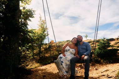 Dağlarda salıncakta sallanan bir çift, arka planda büyüleyici doğal manzarayla öpüşüyorlar. Seyahat, romantizm, yaşam tarzı ve macera temaları için mükemmel