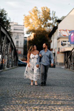 Bir kaldırım taşı caddesinde birlikte yürüyen romantik bir çift, birbirlerine sarılıyorlar ve sevgiyle gülümsüyorlar. Yaşam tarzı, romantizm, seyahat ve ilişki temaları için mükemmel