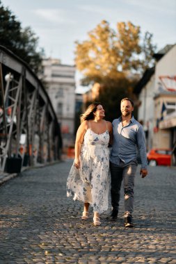 Bir kaldırım taşı caddesinde birlikte yürüyen romantik bir çift, birbirlerine sarılıyorlar ve sevgiyle gülümsüyorlar. Yaşam tarzı, romantizm, seyahat ve ilişki temaları için mükemmel