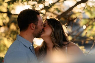 Genç çift, sıcak akşam güneşinde romantik bir öpücük paylaşıyor. Aşkı, samimiyeti ve mutluluğu simgeliyor. Yaşam tarzı, ilişki ve sevgililer günü temaları için mükemmel.